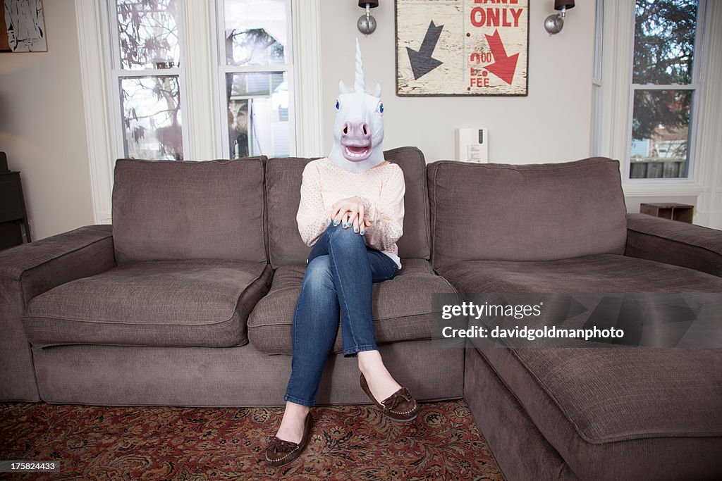 Girl sitting on sofa wearing unicorn head mask