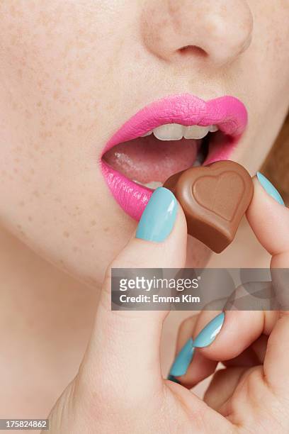 woman wearing pink lipstick eating heart shaped chocolate - lipstick heart stock pictures, royalty-free photos & images
