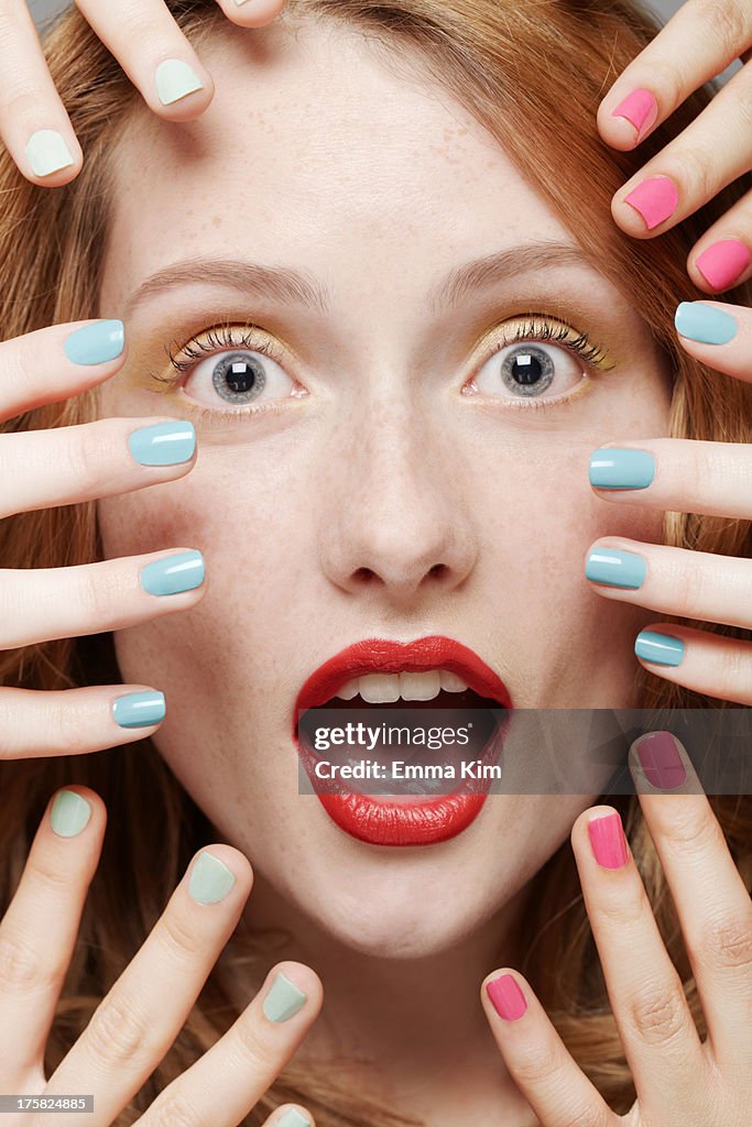 Close up of young woman, eyes and mouth open wide, with fingers around her face