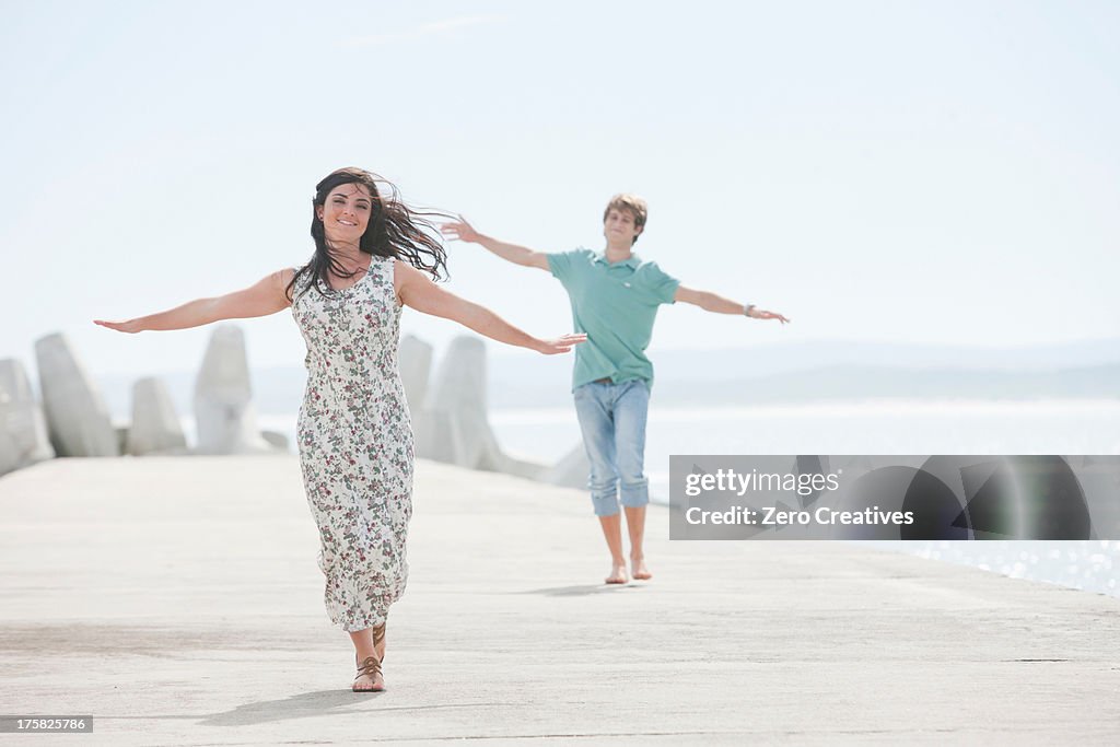 Happy young couple with arms outstretched on pier
