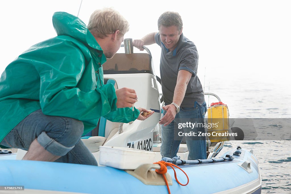 Two young men looking at fishing bait in dinghy