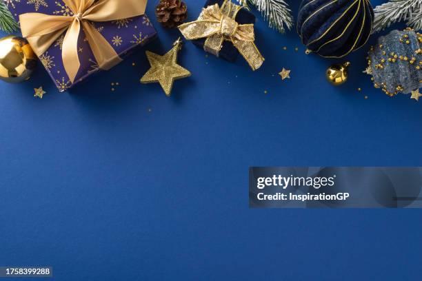 Shining Holiday Magic: Overhead photo of twinkling wrapped gifts, ornaments, evergreen twigs with frost accents on luxurious blue background, with unoccupied spot for your festive greeting or advert