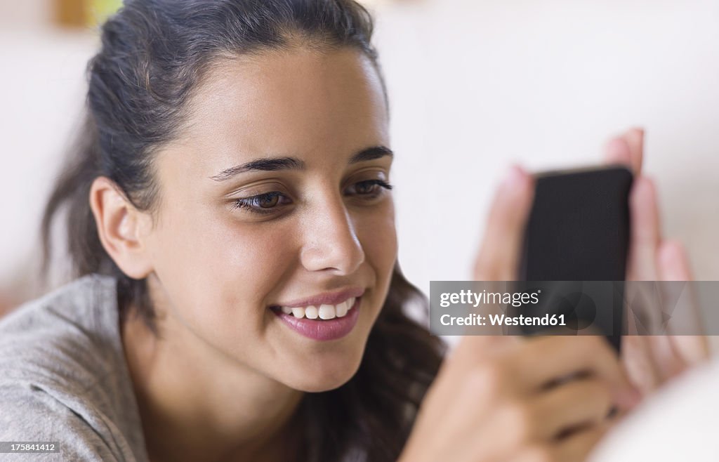 Teenage girl lying on white couch and using smart phone, close up
