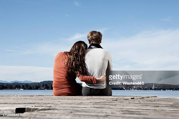 germany, bavaria, couple sitting on jetty at lake starnberg - bergsteiger stockfoto's en -beelden