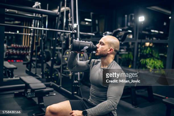 muscular men drink his nutritional supplement in gym - nutritional supplement stockfoto's en -beelden