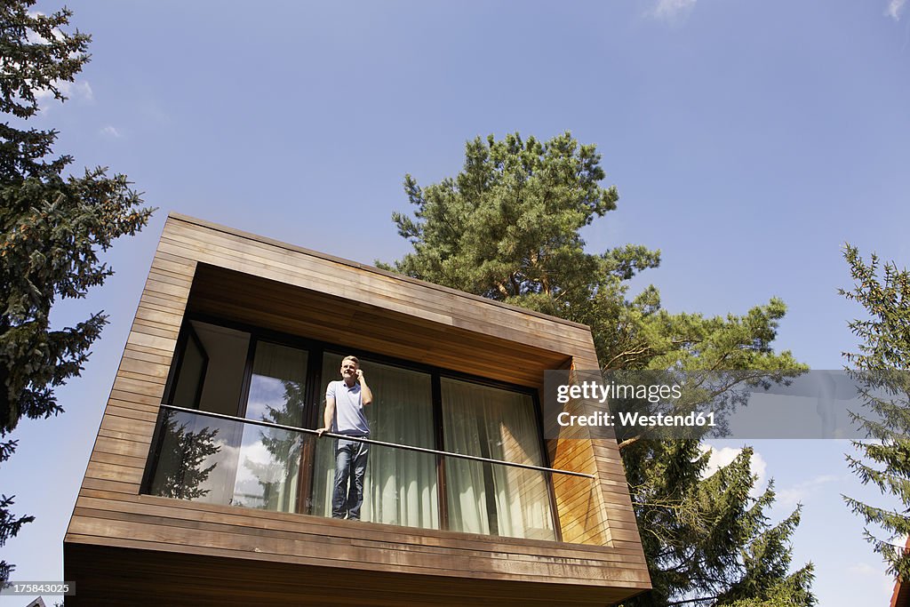 Germany, Berlin, Mature man standing on balcony with mobile phone