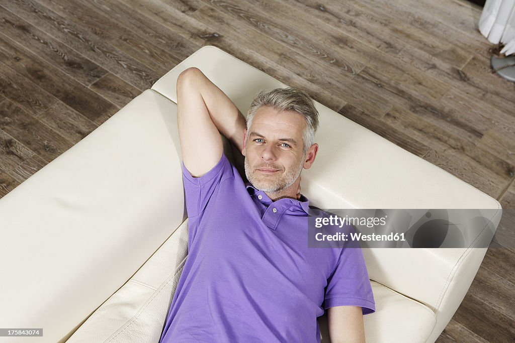 Germany, Berlin, Mature man lying on sofa, smiling, portrait