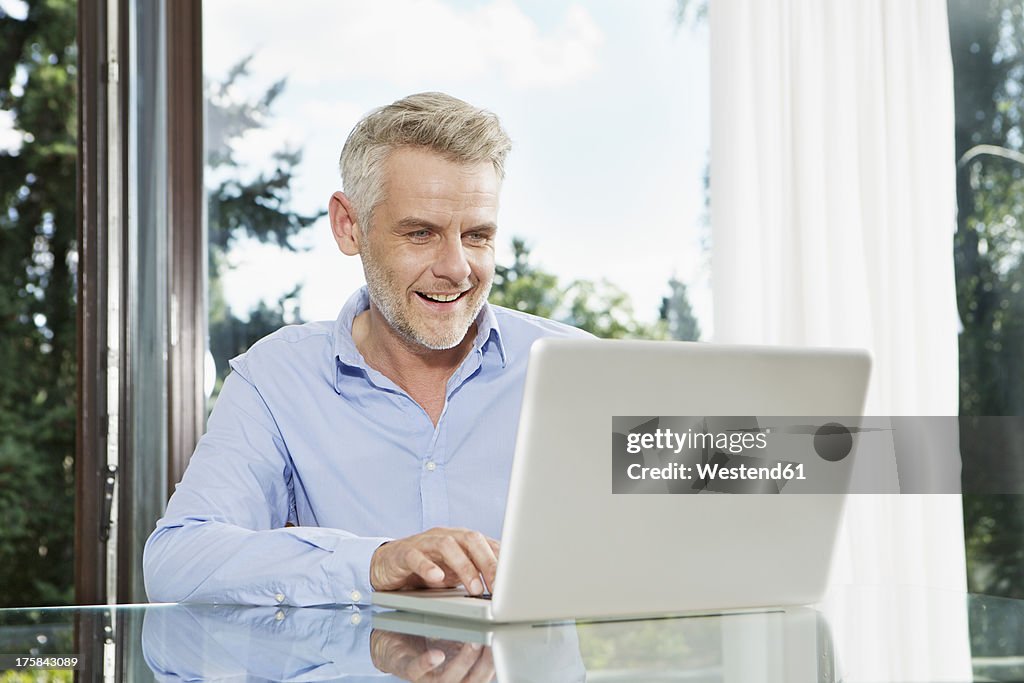 Germany, Berlin, Mature man sitting at table and using laptop