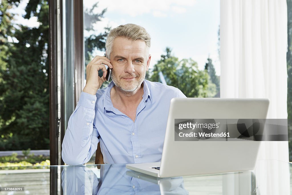 Germany, Berlin, Mature man talking on mobile phone, smiling