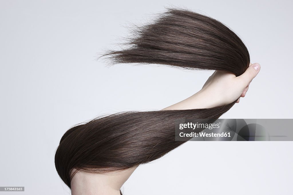 Human hand holding brown hair against white background, close up
