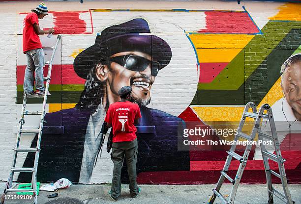 Lead Artist Aniekan Udofia, center, with the help of apprentice Joseph Patino, left, create a mural on the side of Ben's Chili Bowl featuring noted...