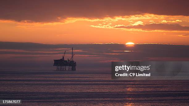 North Sea oil rig or gas platform somewhere off the east coast of the UK. The sun setting behind clouds on the horizon.
