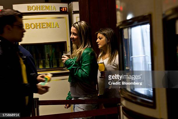 Two women hold glasses of Cia. De Bebidas das Americas Bohemia brand beer while a man prepares to pay his bill at a restored Bohemia brewery in...