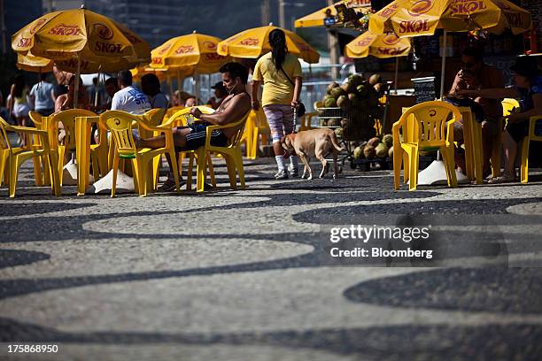 People relax at tables with umbrellas bearing the logo for Cia. De Bebidas das Americass Skol brand beer at Ipanema beach in Rio de Janeiro, Brazil,...