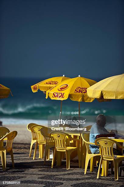 Tables and umbrellas displaying the logo for Cia. De Bebidas das Americass Skol brand beer sit near Ipanema beach in Rio de Janeiro, Brazil, on...