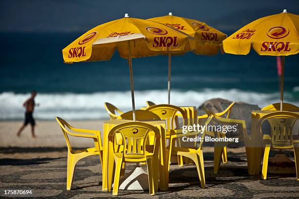 Man jogs on Ipanema beach near tables and umbrellas displaying the logo for Cia. De Bebidas das Americass Skol brand beer in Rio de Janeiro, Brazil,...