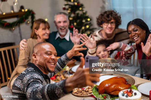 multi-ethnic family using mobile phone video call online to relative. attractive diverse group of people having dinner eating food to celebrate holiday thanksgiving, x-mas eve on dining table at home. - thanksgiving golf foto e immagini stock