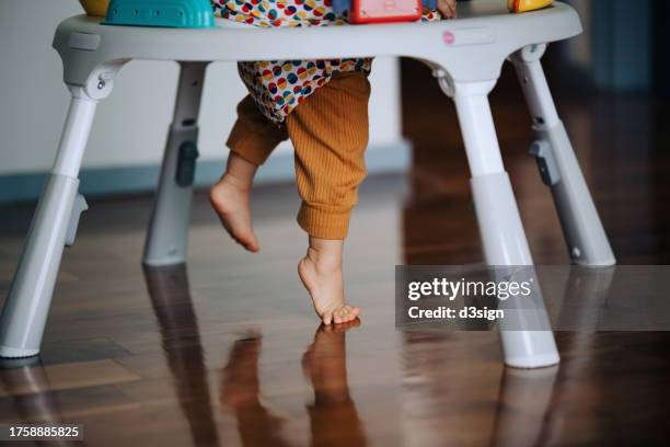 close up of a baby playing in activity centre at home, learning to walk. low section of a baby learning to take her first step in life. first steps of a baby. baby's growth and development concept - primeiros passos imagens e fotografias de stock