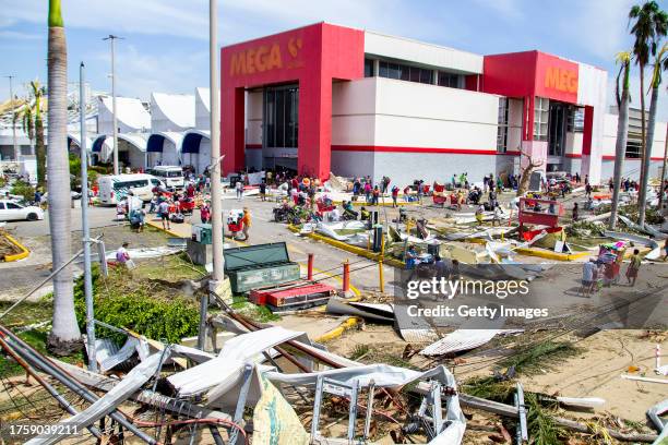 People walk through a parking lot carrying goods from a looted store after hurricane Otis hit Acapulco on October 26, 2023 in Acapulco, Mexico. Otis...