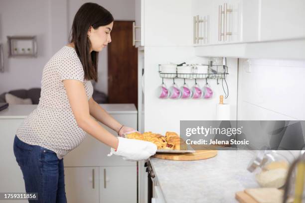 eine schwangere frau stellt ein heißes tablett auf die arbeitsplatte. - lady cooking confused stock-fotos und bilder