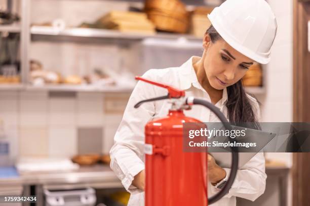 a female safety inspector checks the fire extinguishers in the hotel kitchen. - fire extinguisher inspection stock pictures, royalty-free photos & images