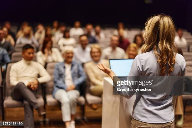 vista trasera de una oradora dando un discurso frente a la gente en el centro de convenciones. - announcement fotografías e imágenes de stock