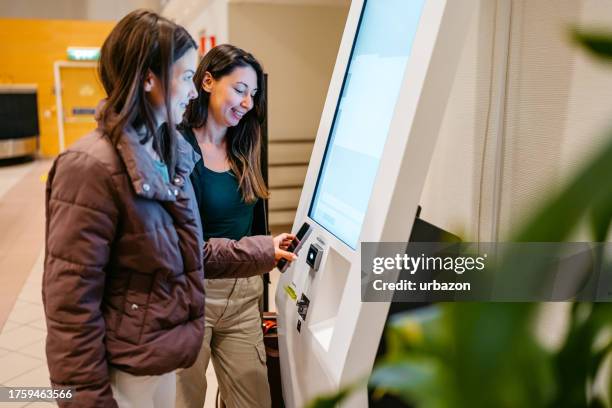 two female friends checking-in their airplane tickets at the airport - self service stock pictures, royalty-free photos & images