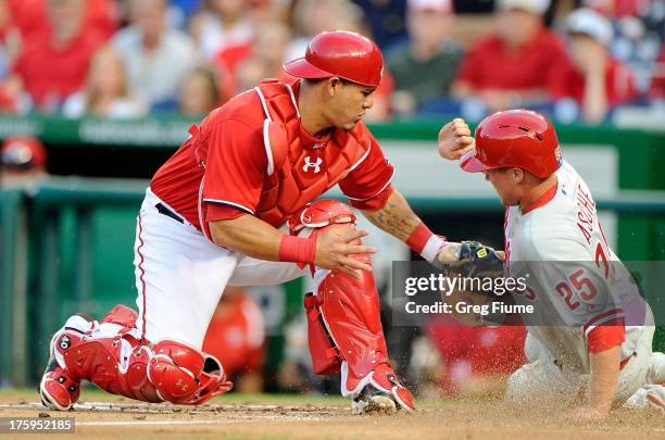 Cody Asche of the Philadelphia Phillies knocks the ball away and scores in the second inning against Wilson Ramos of the Washington Nationals at...