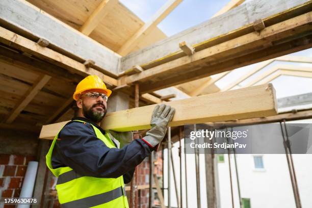 maschio caucasico, che trasporta un legname, mentre lavora in un cantiere - imprenditore edile foto e immagini stock