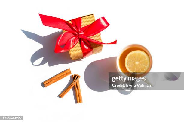 christmas design with craft gift box with red ribbon, cinnamon sticks and cup of tea with lemon on white background. - ribbon worm stock pictures, royalty-free photos & images