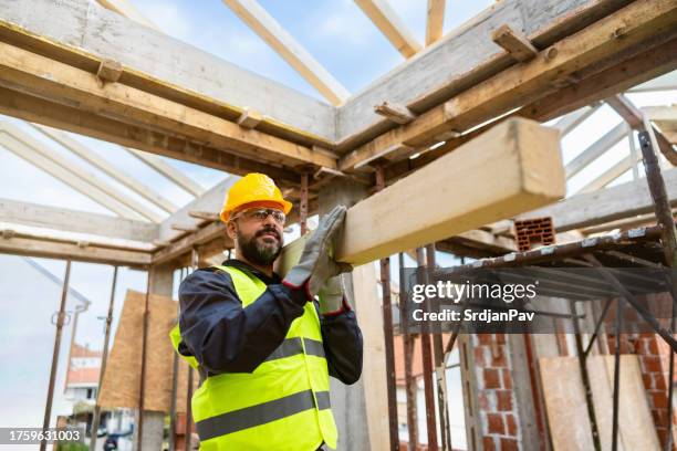 caucasian male roofer, carrying an timber, while working on a construction site - dakdekker stockfoto's en -beelden