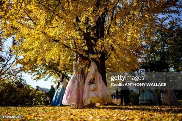 Women wearing traditional Hanbok dresses pose for a selfie under a gingko tree with autumnal foliage in the Gyeongbokgung Palace grounds in Seoul on...