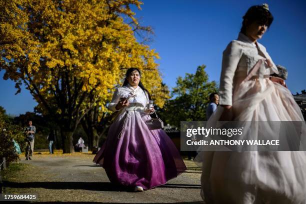 Women wearing traditional Hanbok dresses walk in front of a gingko tree with autumnal foliage as they visit the Gyeongbokgung Palace grounds in Seoul...