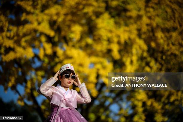 Woman wearing a traditional Hanbok dress poses for a photo near a gingko tree with autumnal foliage in the Gyeongbokgung Palace grounds in Seoul on...