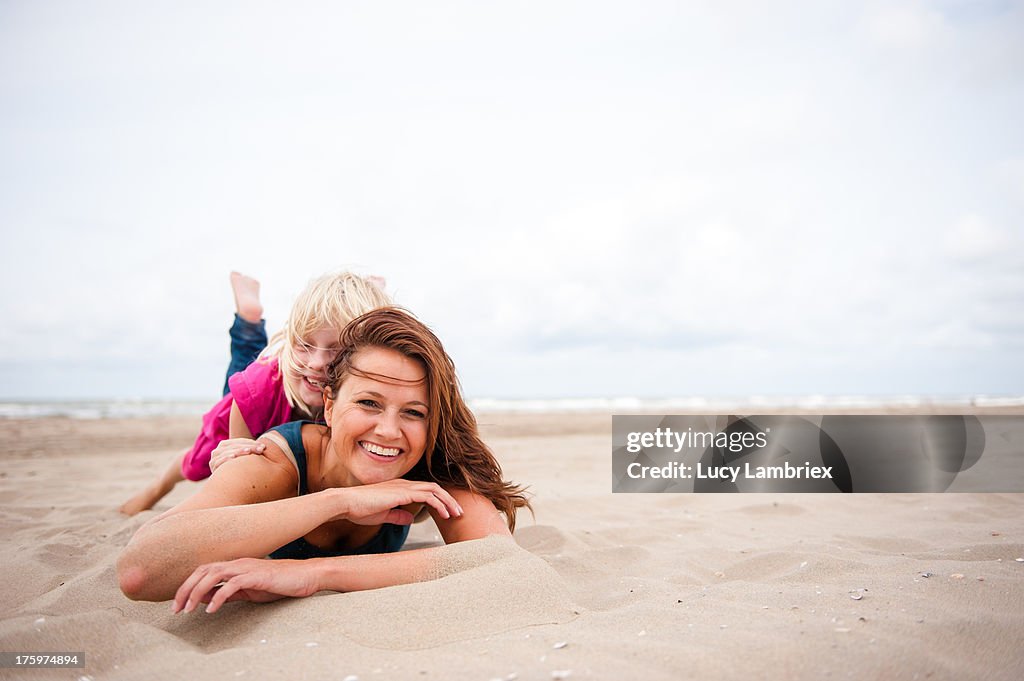 Mother lying on the beach with her daughter on top