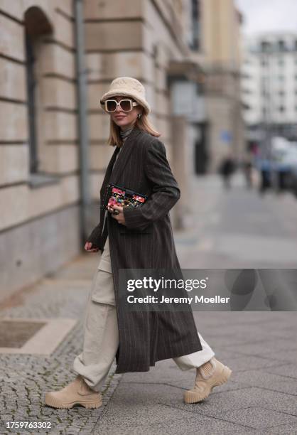 Sonia Lyson seen wearing Louis Vuitton light beige sunglasses, Louis Vuitton light beige fluffy bucket hat, Louis Vuitton Malle colorful clutch bag,...