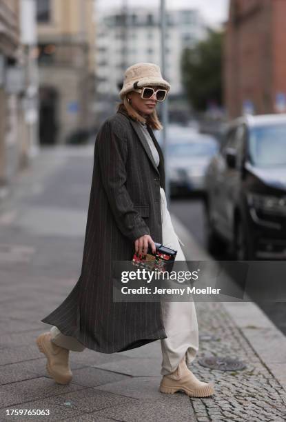 Sonia Lyson seen wearing Louis Vuitton light beige sunglasses, Louis Vuitton light beige fluffy bucket hat, Louis Vuitton Malle colorful clutch bag,...