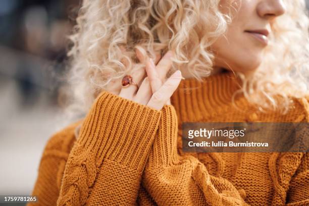 cropped photo of charming woman with curly hair and orange sweater standing amid city street - frau haarsträhne blond beauty stock-fotos und bilder