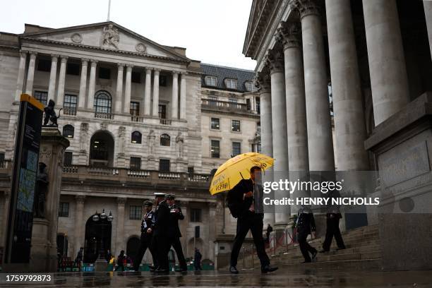 Pedestrian with an umbrella walks by the Bank of England building and Royal Exchange building , in the financial district, central London, on...