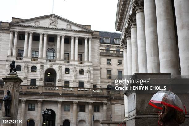 Pedestrian with an umbrella walks by the Bank of England building and Royal Exchange building , in the financial district, central London, on...
