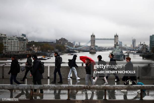 Pedestrians walk over the London Bridge with Tower Bridge on the background, in London, on November 2, 2023.