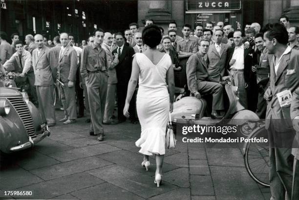 Young actress and circus performer Moira Orfei walks towards the Galleria Vittorio Emanuele II in Milan, Italy, while a large group of men turn to...