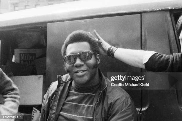 An African American having his hair stroked by someone's extended arm on Broadway on the Upper West Side of New York City, 1971.