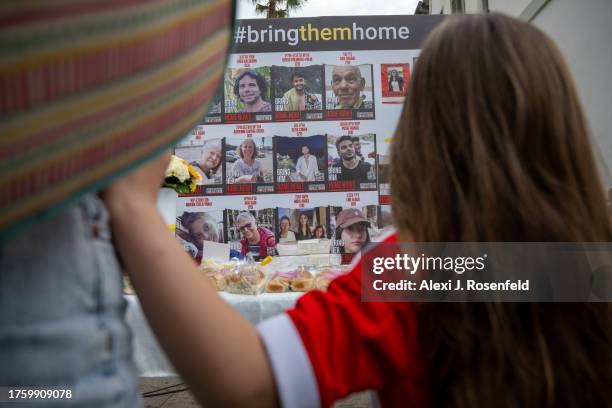 Girl grabs holds onto her mother while looking at a wall with photos of those kidnapped aftern a special ‘Kabalat Shabbat,’ prayer service outside...