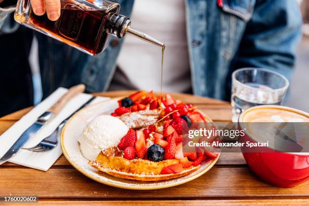 man pouring maple syrup on waffles with fresh berries and ice cream - paris cafe stock pictures, royalty-free photos & images