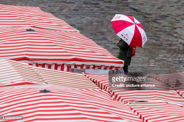 November 2023, Bavaria, Nuremberg: A woman walks in rainy weather with an umbrella across the main market past the red and white striped roofs of the...