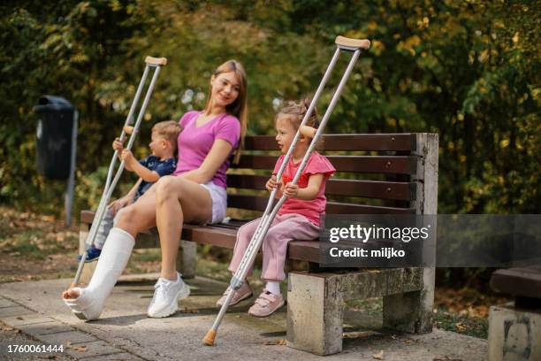 frau mit gips am bein verbringt zeit mit zwei kindern im park - gebrochenes bein stock-fotos und bilder