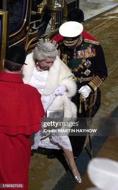 Britain's Queen Elizabeth II has to reach out to avoid the sand spread out on the road as she arrives at the House of Lords, 26 November 2003, for...