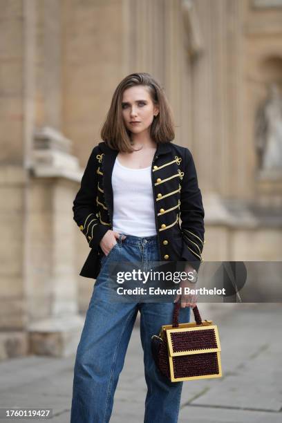 Iana Rad wears a black and gold military jacket with golden buttons and stripes, a white t-shirt, blue denim pants / jeans, a Rolex watch, a golden...