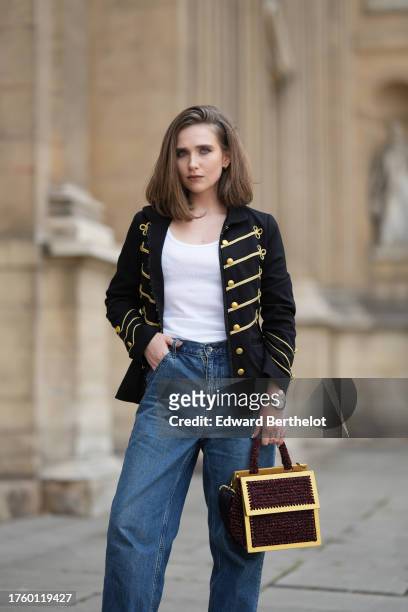 Iana Rad wears a black and gold military jacket with golden buttons and stripes, a white t-shirt, blue denim pants / jeans, a Rolex watch, a golden...